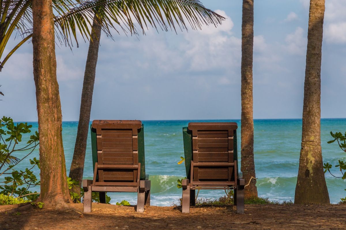 A typical beautiful holiday scene with two beach chairs, flanked by palm trees, offering a great ocean view of the East Coast in Malaysia.
